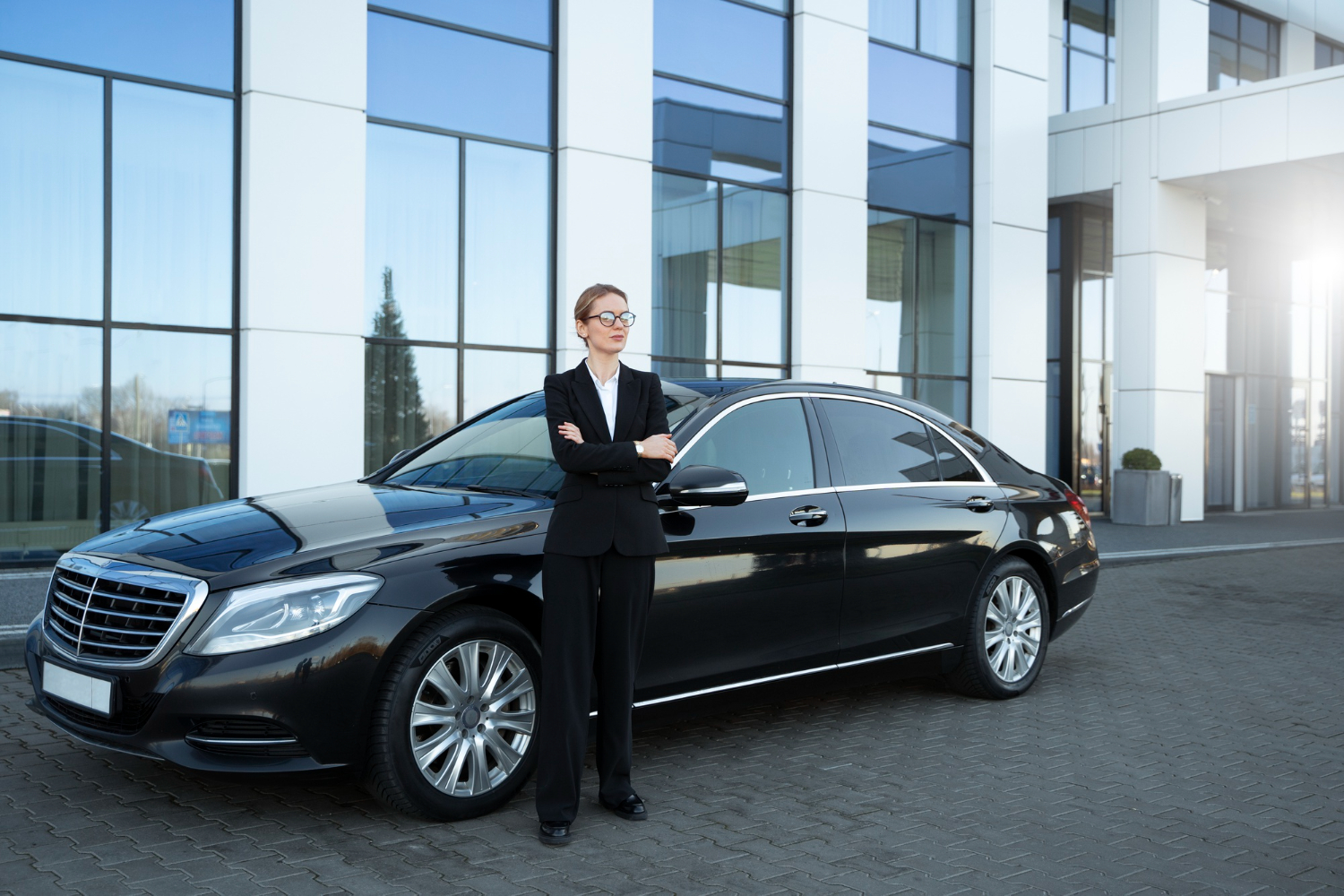 Professional chauffeur in business attire beside an executive sedan outside a modern Boston office building